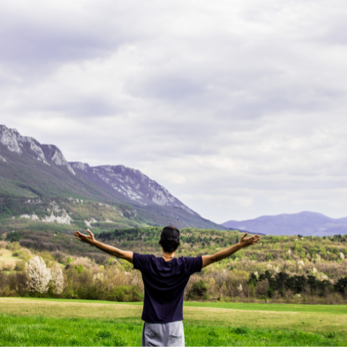 An individual in a field, arms extended, enjoying the serenity of the outdoors and connecting with the environment.